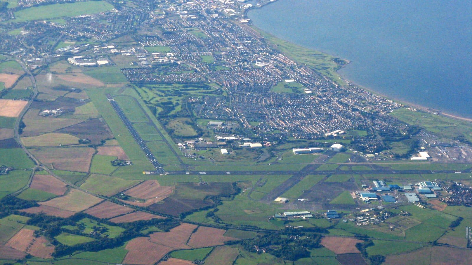 Vue aérienne de Prestwick, en Écosse, et de son aéroport : pistes, champs, ville et littoral